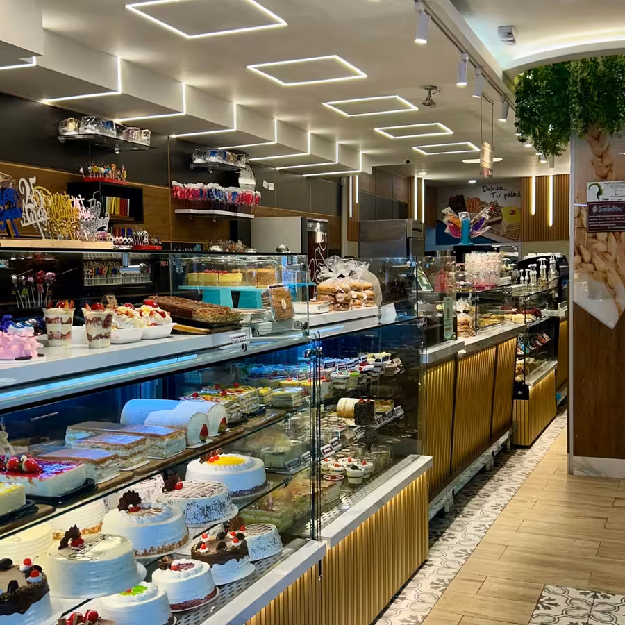 Interior de la sede de la Calle 72: vitrinas refrigeradas llenas de tortas, piso de madera y luces de techo