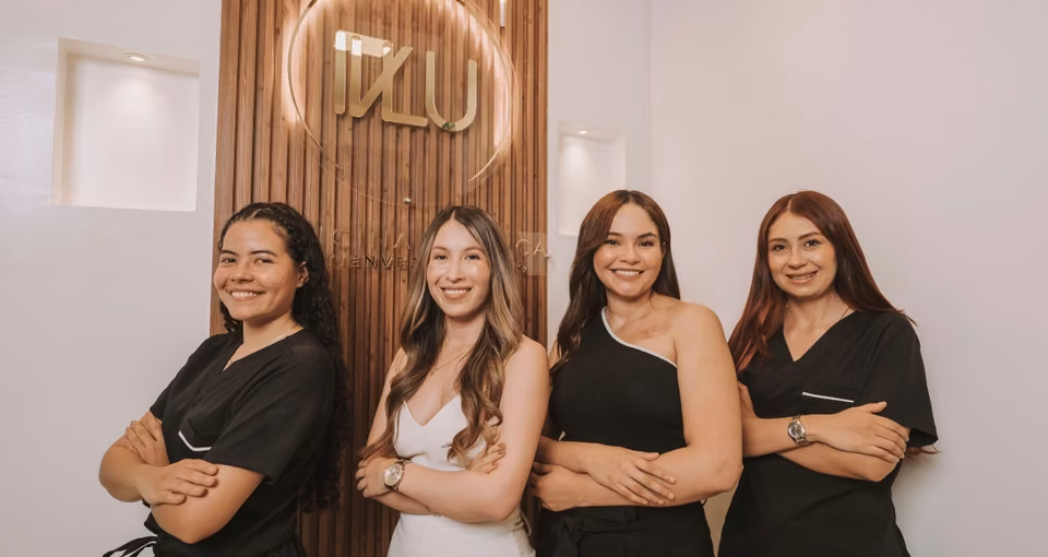 Team of four women with crossed arms in front of the wood wall with the illuminated IVLU logo