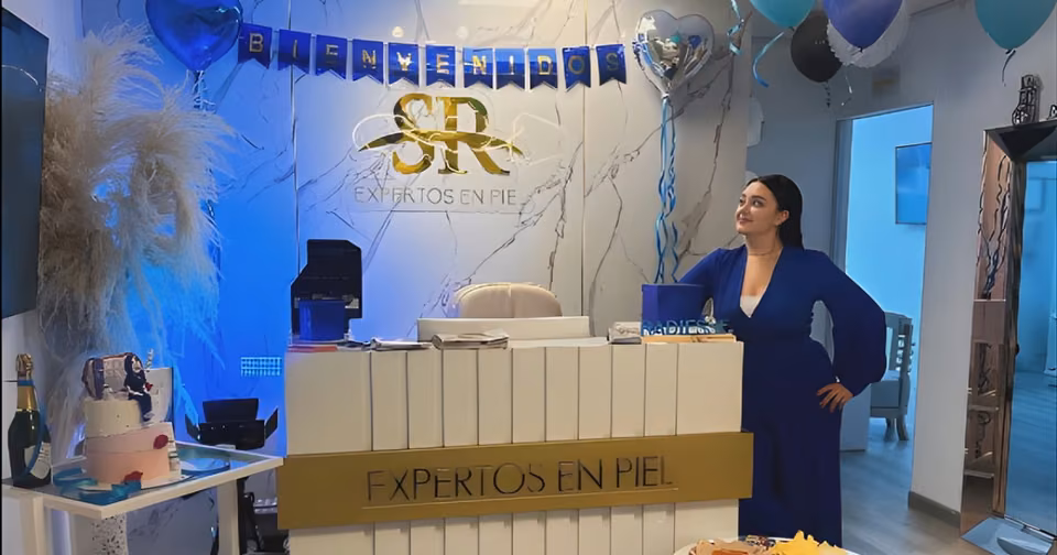 La Dra. Stefania Rincón, con vestido azul, junto a la recepción con el letrero dorado «Expertos en Piel» y el logo SR en la pared