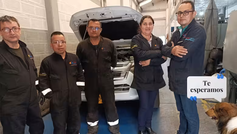 Cinco integrantes del equipo con overol oscuro frente a una camioneta con el capó abierto en el taller, junto a un perro y un letrero «Te esperamos»